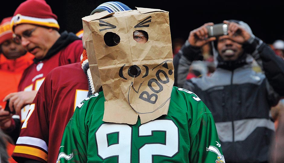 Football fan wearing a green jersey and a paper bag mask with drawn eyes and a mouth, expressing discontent.
