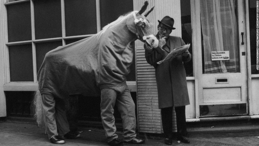 A man reading a newspaper next to a person in a horse costume, showcasing a unique interaction in a vintage setting.