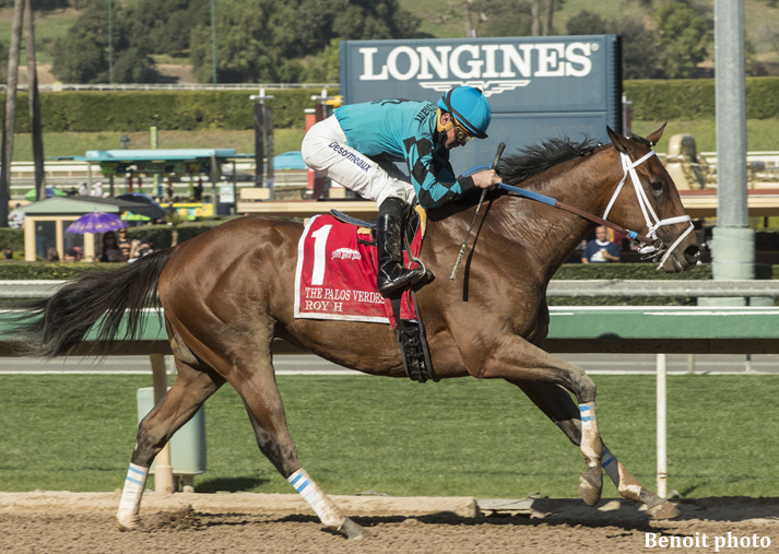 Racehorse Roy H with jockey in teal silks racing on a dirt track at a horse racing event.