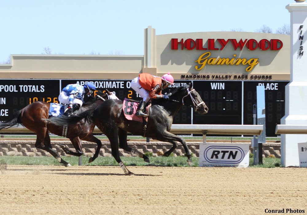 Two horses racing at Mahoning Valley Race Course with a gaming facility in the background.