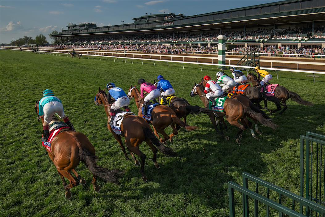 Horses racing on a turf track with jockeys in colorful silks during a competition.