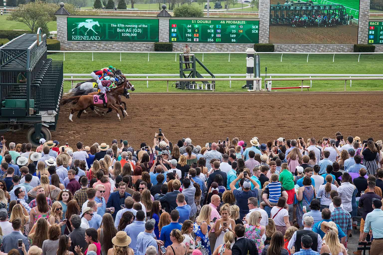 Horses racing at Keeneland Racecourse with a large crowd watching the event.