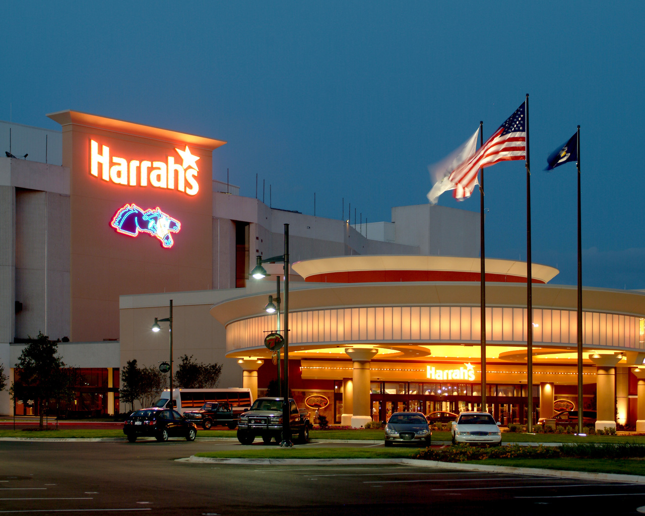 Exterior view of Harrah's Casino entrance with illuminated signage and flags at night.