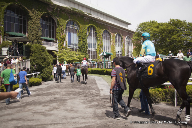 Jockeys and horses walking towards the racetrack at Belmont Park during a horse racing event.