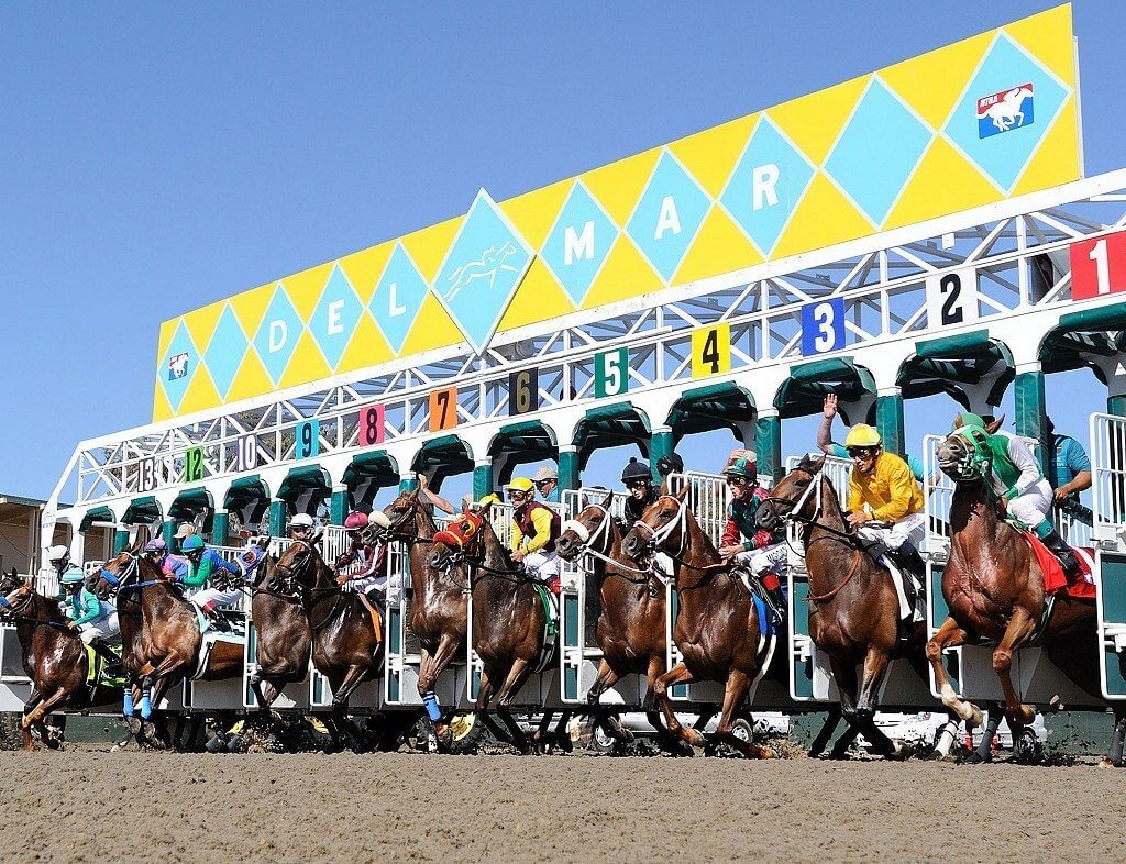 Exciting start of a horse race at Del Mar racetrack with multiple horses and jockeys in action.