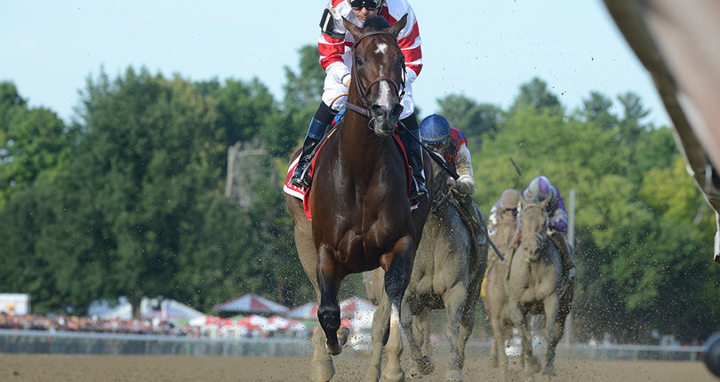 A racehorse with a jockey in red and white silks running on a dirt track during a race.