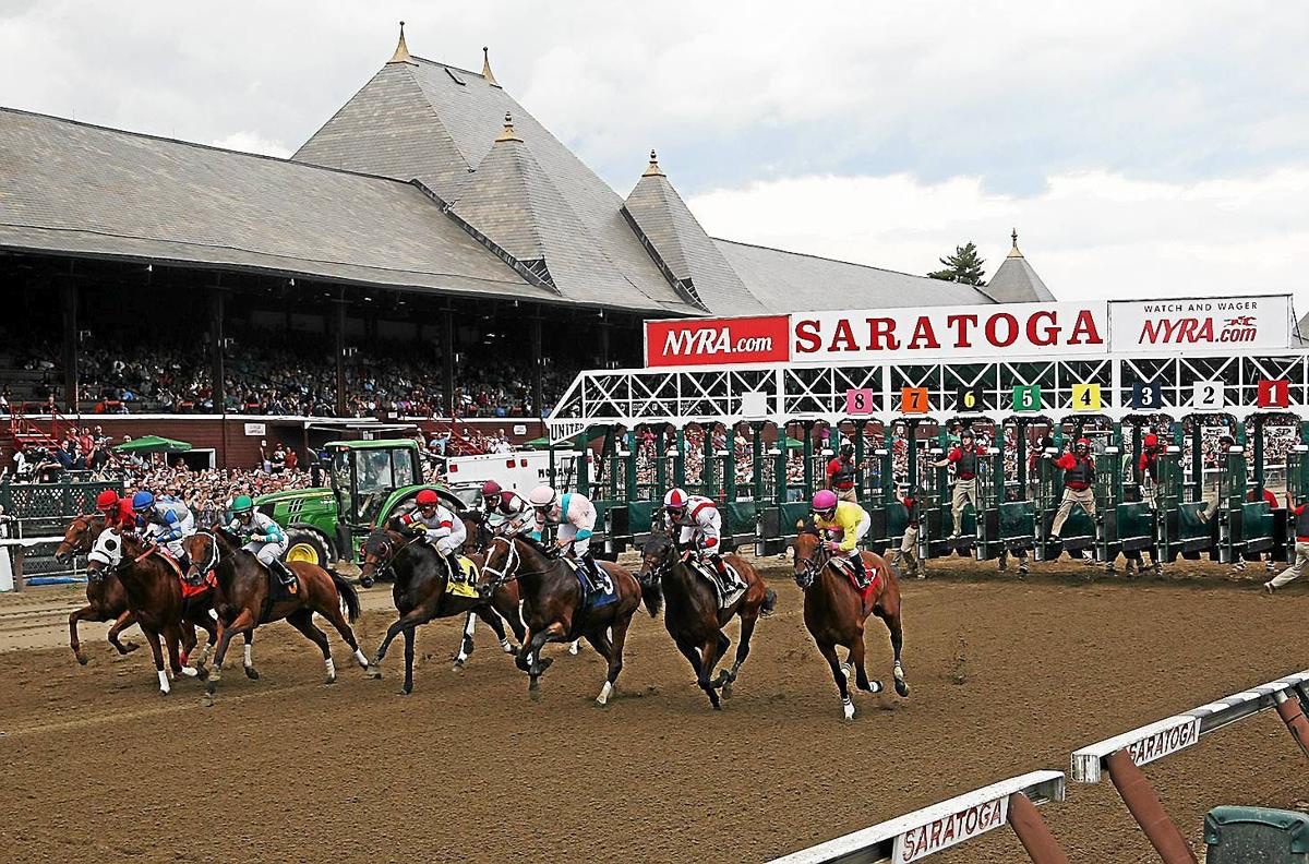 Horses and jockeys racing at the Saratoga Race Course with starting gates in view.