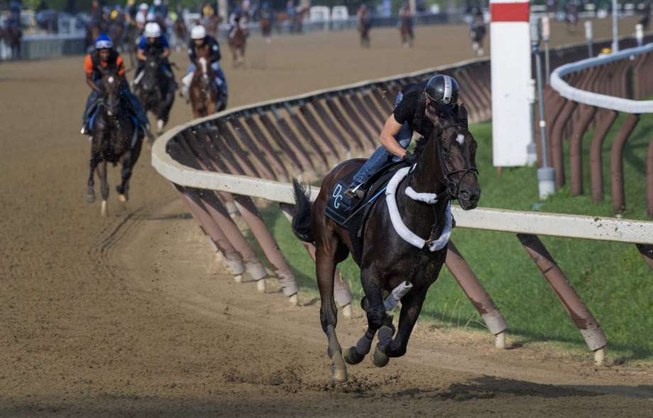 A black racehorse galloping on a dirt track with jockey in a helmet and other horses in the background.