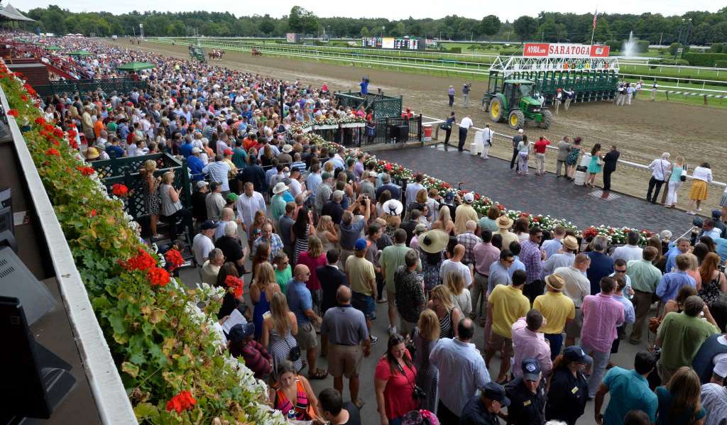 Large crowd gathered at Saratoga Race Course with horses and jockeys preparing for a race.