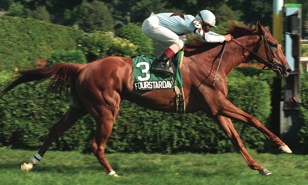 A jockey riding a chestnut horse named Fourstardave during a race on a grassy track.