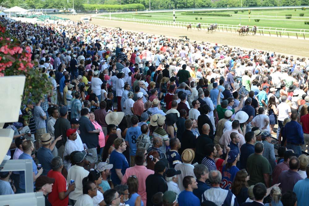 Large crowd of spectators gathered at a horse racing event, observing the race on the track.