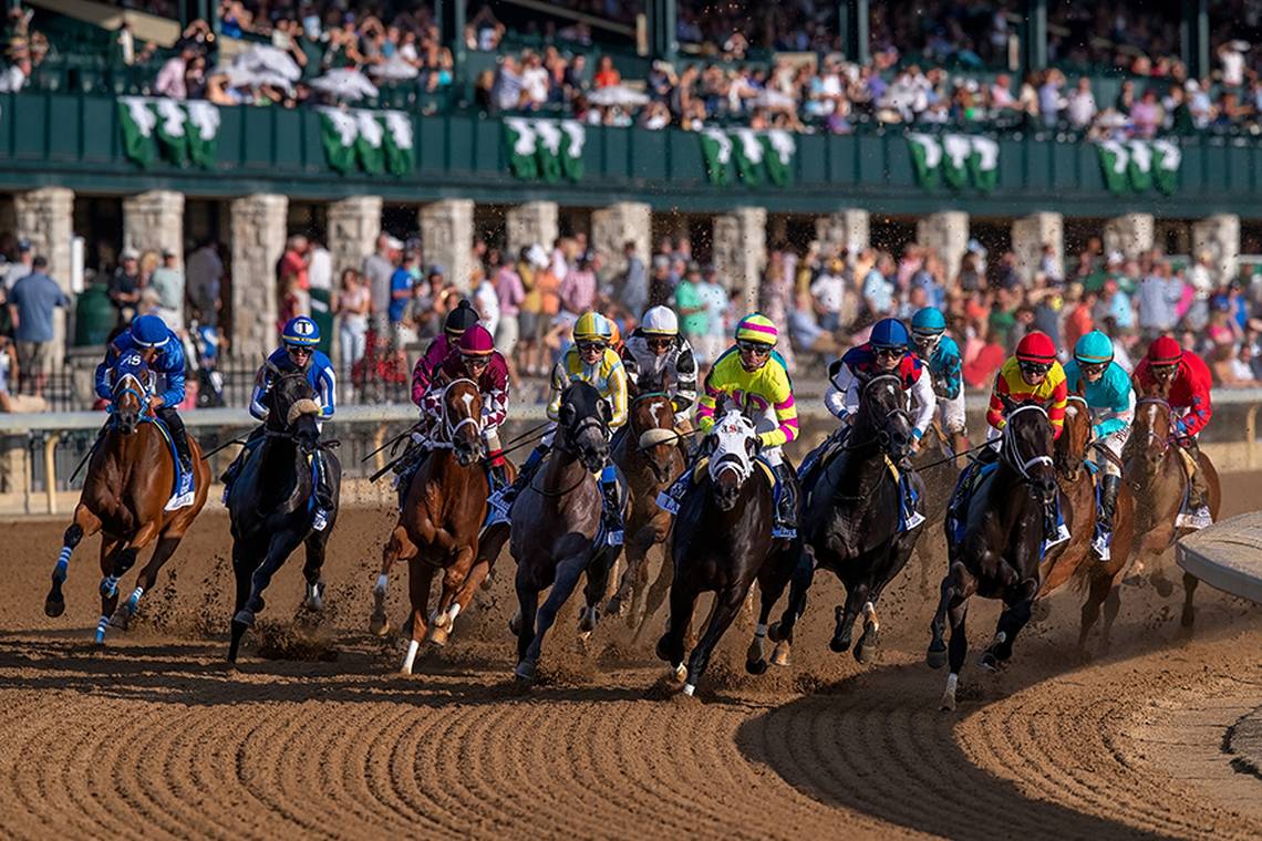 A group of racehorses with jockeys in colorful silks competing on a dirt racetrack.