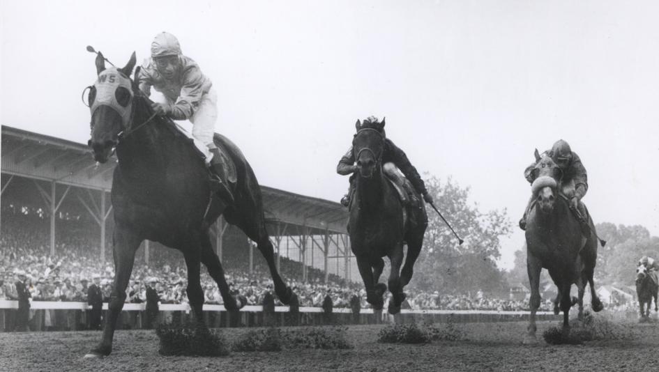 Black and white image of horses racing at a track with jockeys, showcasing the excitement of horse racing events.