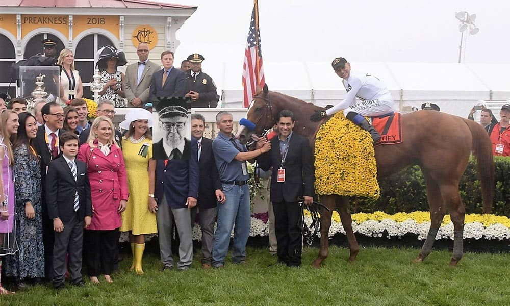 Celebration of the 2018 Preakness Stakes winner with a horse adorned in flowers and a crowd of people in formal attire.